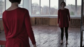 Young girl in red dress 
is dancing in front of the mirror in the dance studio. Contemporary dance in the studio. 4K video in slow motion. 