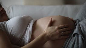 Close-up of the pregnant woman's belly while she's stroking and touching it with her hand at home. Slow motion video
