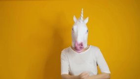 Weird funny video - woman with unicorn head dancing over yellow background