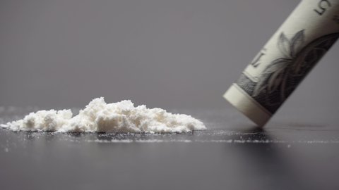 Drug Abuse. A rolled banknote snorting a line of cocaine powder. Problems with drugs concept. Grey background. Close-up macro shot.