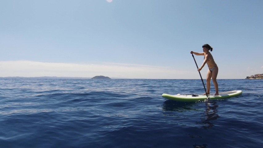 A sportive girl in her twenties wearing swimwear doing water sports. Outdoor stand up paddling in Greece on a sunny day.