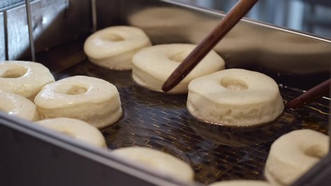 The chef is turning the donuts on another side with sticks while frying. The donuts are very soft.