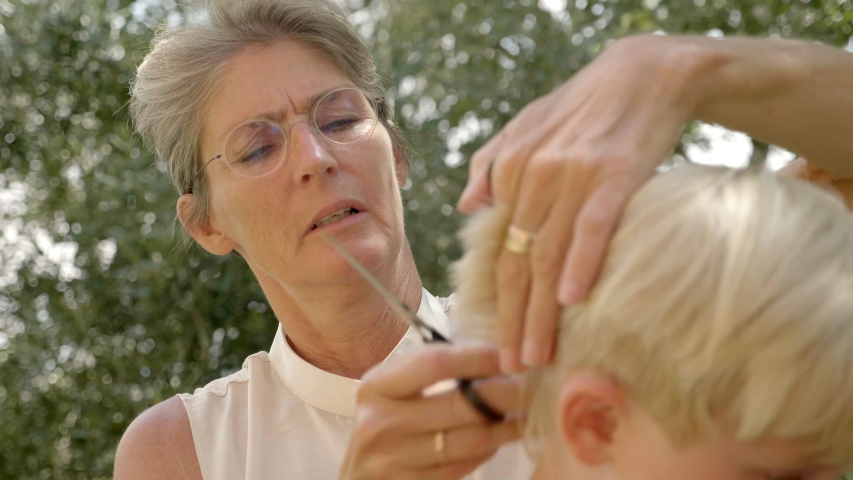 A slow-motion picture of a mother giving her son a hair cut outside.