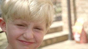 A slow-motion video of a happy blonde boy having his hair cut while looking at the camera.