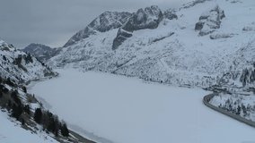 Aerial Drone footage winter view of Fedaia Dam lake with snow in Dolomites Alps Italy // no video editing