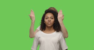 Funny girl cover face of friend with her hands and smiling on chroma key background . Happy multiracial women having fun on a Green Screen, 4k video footage slow motion 60 fps