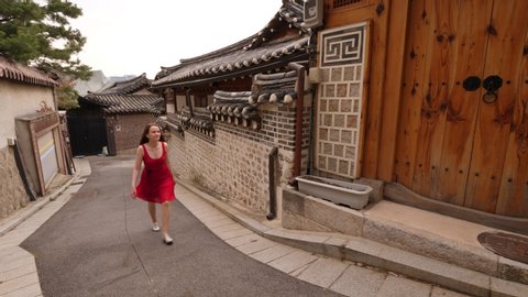 Young woman walk at empty street of Bukchon Hanok Village, tracking camera motion. Tourist girl explore traditional Korean village in heart of Seoul city. Low rise renovated houses around