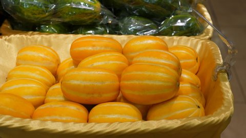 Ripe yellow oriental melon at stall of Korean supermarket, woman hand take one chamoe fruit. Popular product at Asia, small colorful striped plants stacked in container