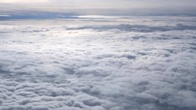 Aerial view above cloudscape from cabin. White fluffy clouds in blue sky, top view. Flying over soft light cloud, looking through air plane window