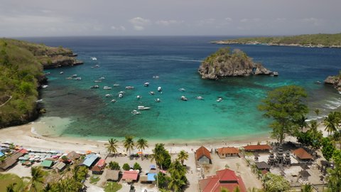 Aerial drone flight over paradise beach at Nusa Penida island, Bali, Indonesia, 4k. Sunbeds and umbrellas on the white sand. Water in the lagoon is very clear and bright, turqoise, green, emerald