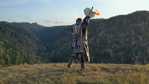 Siberian shaman performs a ritual dance and beats a tambourine on the top of the mountain.