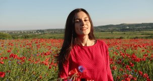 Incredible brunette woman circling and having fun through a poppy field. Charming lady in a red polka dot dress with bouquet of poppies in hands. 4K video.