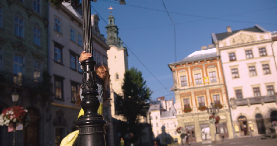 Attractive happy girl with long blond hair in a denim jacket, yellow jersey and with a yellow backpack spinning around and smiling. slow motion