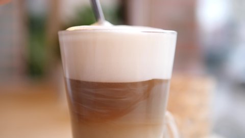 Stirring Thick Foam Of Hot Coffee Latte With Spoon In A Glass Cup.