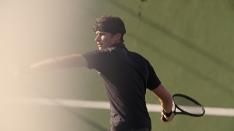Professional tennis player hitting forehands strokes on hard court. Fit young man in sportswear playing tennis on hard court on a sunny day.