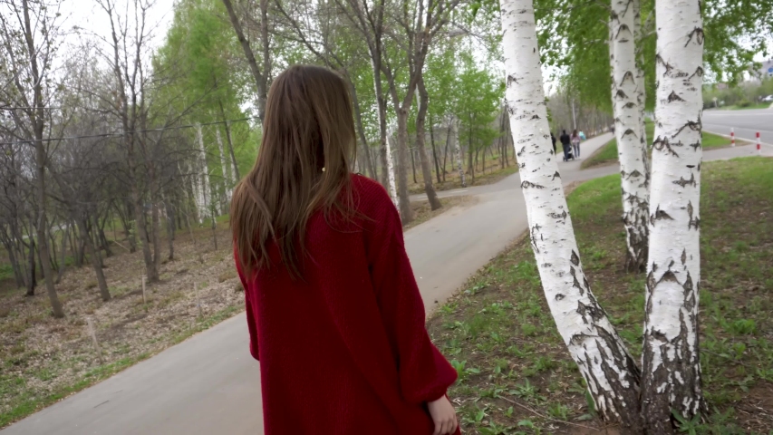 A young girl walks on a green grove and touches young trees. gently puts his hands on the bark and runs his fingers over it. she leans against a tree