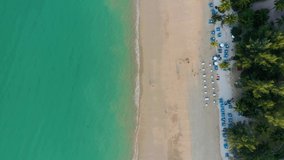 Tropical beach, umbrellas and boats with people on vacation. Aerial drone video