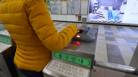 SEOUL, SOUTH KOREA - MARCH 31, 2018: Woman pay fare using smart ticket, exit through metro station gate. Close shot of reader device on top of turnstile, green arrow at front of booth show direction