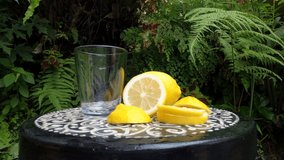 Pouring Organic Juice Of Yellow Fresh Lemon in a Glass With The Slices On The Round Table Outdoor For Healthy Life, Nutrition And Herbal Medicine Consume By Vegetarian, RAW Full HD And 4K Video. 