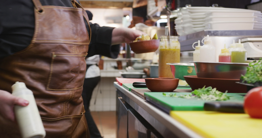 Side view of a Caucasian female cook working in a busy restaurant kitchen, garnishing potato salad, her male colleague working in the background Royalty-Free Stock Footage #1045617850