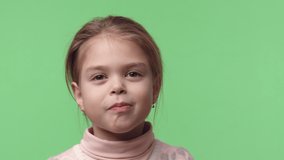 Video portrait of little happy actress send an air kiss. Sweet smiling baby girl dressed in pink sweater with gold earrings. In studio beautiful baby stand on green chroma key background.