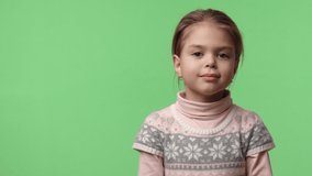 Video portrait of happy baby girl 6 years old in studio shows heart gesture by two hands, looking at camera. Sweet caucasian baby dressed in pink sweater stays on green chroma key background.