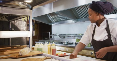Side view of a Caucasian male chef working in a busy restaurant kitchen, checking orders, a female African American cook garnishing food on plates ready to be served
