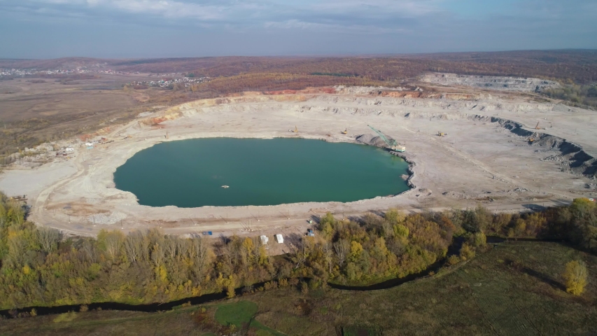 Quarry filled with water surrounded by a summer forest on a beautiful sunny day. Aerial view, 4K.