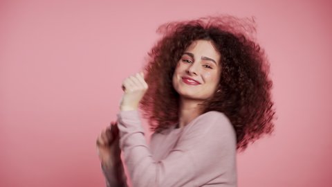 Beautiful woman with curly hair dancing with head on pink studio background. Cute girls portrait. Party, happiness, freedom, youth concept.