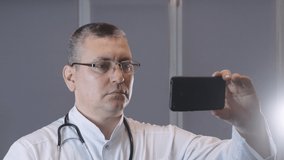 a doctor in uniform with a phonendoscope talks to a patient in a video chat application, video conferencing, online patient consultation, remote medical consultation in an Internet application concept