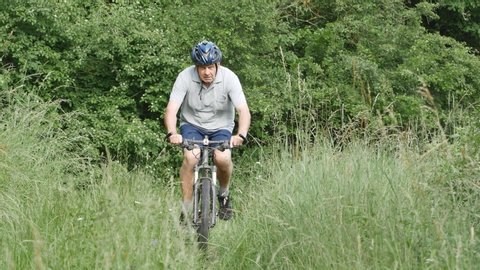 Senior man riding a bike on field path