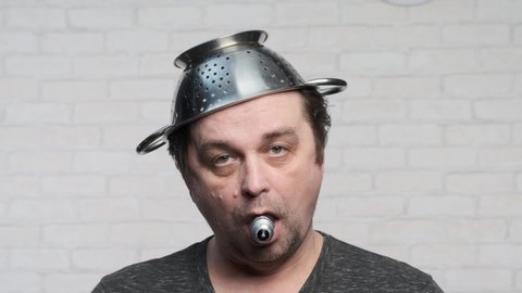 Portrait of adult funny man with colander on his head and light bulb in his mouth.
