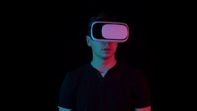 Young man in VR glasses. A man immersed in virtual reality makes movements with his hands. Blue and red light falls on a man on a black background.