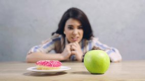 selective focus of apple and doughnut near confused girl