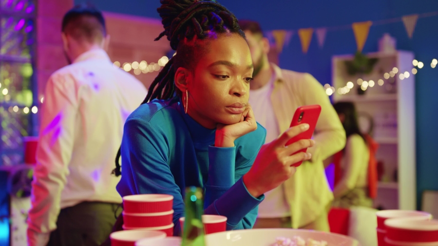 Unhappy afro-american girl in stylish look using smartphone browsing social media of boredom feeling lack of attention on holiday party with friends. Unsociable people concept. | Shutterstock HD Video #1045646017