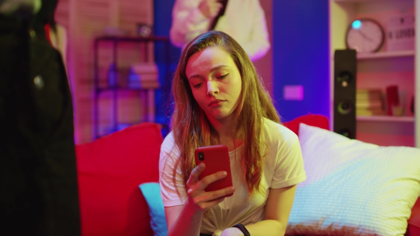 Young pretty woman using a smartphone feeling lack of attention on party. Bored sad girl browsing mobile phone news and sitting on sofa. | Shutterstock HD Video #1045646134