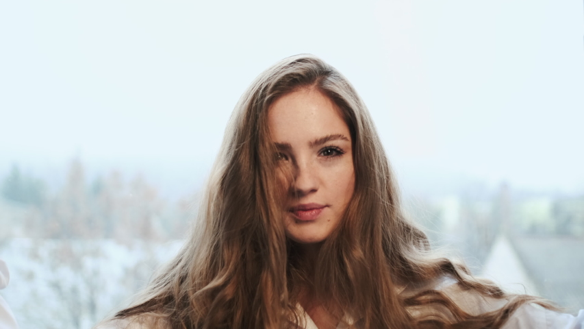 Funny Girl With Long Hair. Girl In White Shirt Puts Her Fingers To The Face. She Jokes.