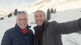 Father and son taking selfie video in snowcapped mountains in winter enjoying ski season vacations together and sharing to friends family with selfie video. Two people enjoying mountains 