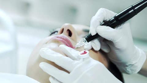 Young woman having permanent makeup on lips in beautician salon.