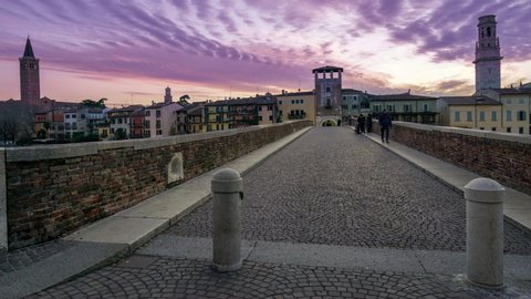 Verona, Italy - January 21, 2020:Sunset in Verona, Italy. Time Lapse of people crossing Ponte Pietra old roman bridge over Adige river.