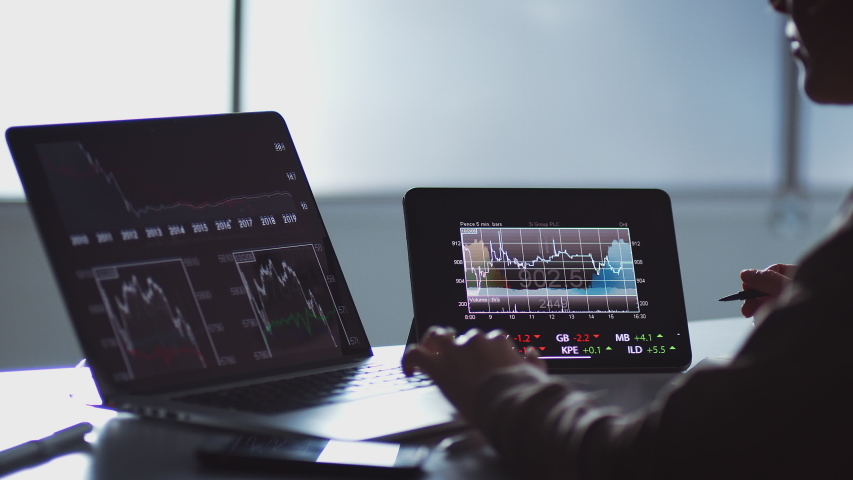 Close up of share trader at desk with stock price data displayed on laptop and digital tablet - shot in slow motion Royalty-Free Stock Footage #1045680607
