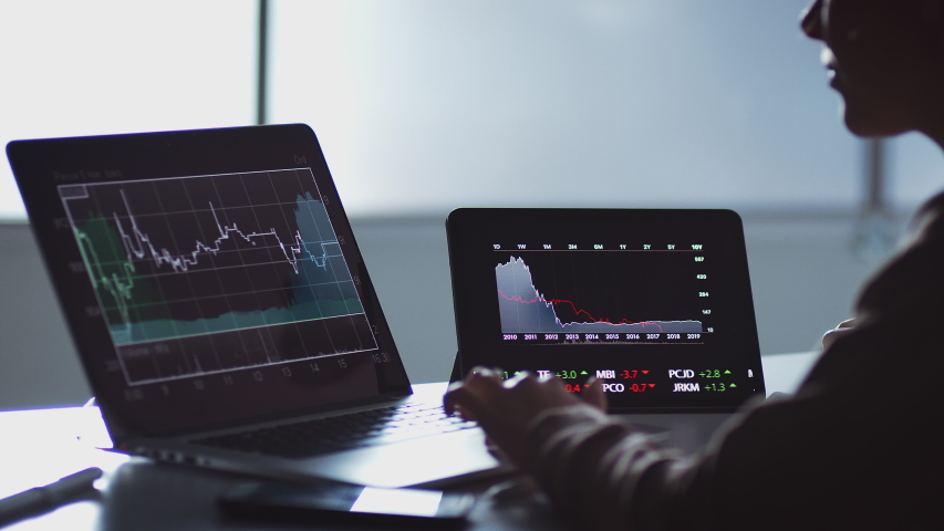 Close up of share trader at desk with stock price data displayed on laptop and digital tablet - shot in slow motion | Shutterstock HD Video #1045680607