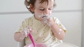 Baby eating. Cheerful baby child eats food itself with hands and spoon. Portrait of beautiful child having breakfast at home. Cute child eating breakfast at home. Little and funny baby eating yogurt