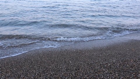 Close-up of sea waves washing ashore a stony beach at evening.
