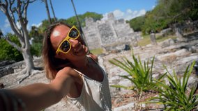 Blond girl visiting Mexico. Young woman taking selfie in front of ancient Mayan temple, daytime. Tropical vacations concept 