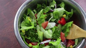 mixing fresh vegetables salad with corn cucumber lettuce red onion tomatoes parsley in metal bowl top view