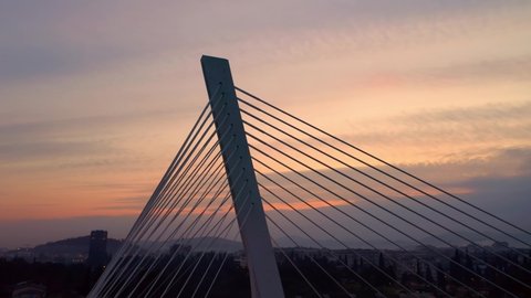 Silhouette of a cable-stayed bridge against colorful sunset sky. Cables (stays) running form the single pylon (tower) form a fan-lake pattern. Millennium bridge in Podgorica, Montenegro. Aerial shot.
