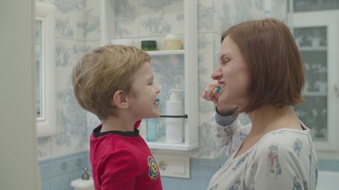 Young mother and preschool boy in red pajamas brushing their teeth. Fun family bath routine. Mother and son laughing in bathroom. 