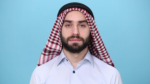 Bearded young arabian muslim man 20s in keffiyeh ring igal casual clothes posing isolated on pastel blue background. People religious lifestyle concept. Looking at camera, charming smile
