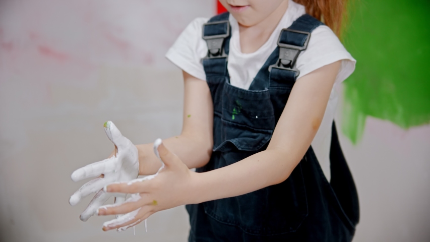 Little girl is examining her hands in white paint